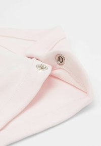 Svetle růžová látka s hladkou texturou, obsahující kulatý límec a stříbrné drukové zapínání. Čistý design s jemným prošitím.