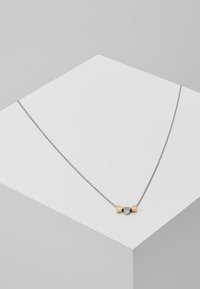 Sølvsnor halskæde med tre hjerteformede vedhæng i guld, sølv og en sølv accent med en central stonedetalje.