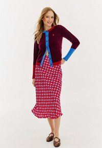 Burgundowy kardigan z niebieskimi i czerwonymi akcentami; guziki z przodu. Spódnica ma czerwone tło z niebieskim wzorem serc, dół jest falbaniasty.