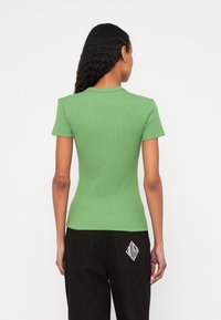 Zielona prążkowana koszulka polo z krótkim rękawem, dopasowany fason z okrągłym kołnierzem, zestawiona z czarnymi luźnymi spodniami z logo w kształcie diamentu na tylniej kieszeni.