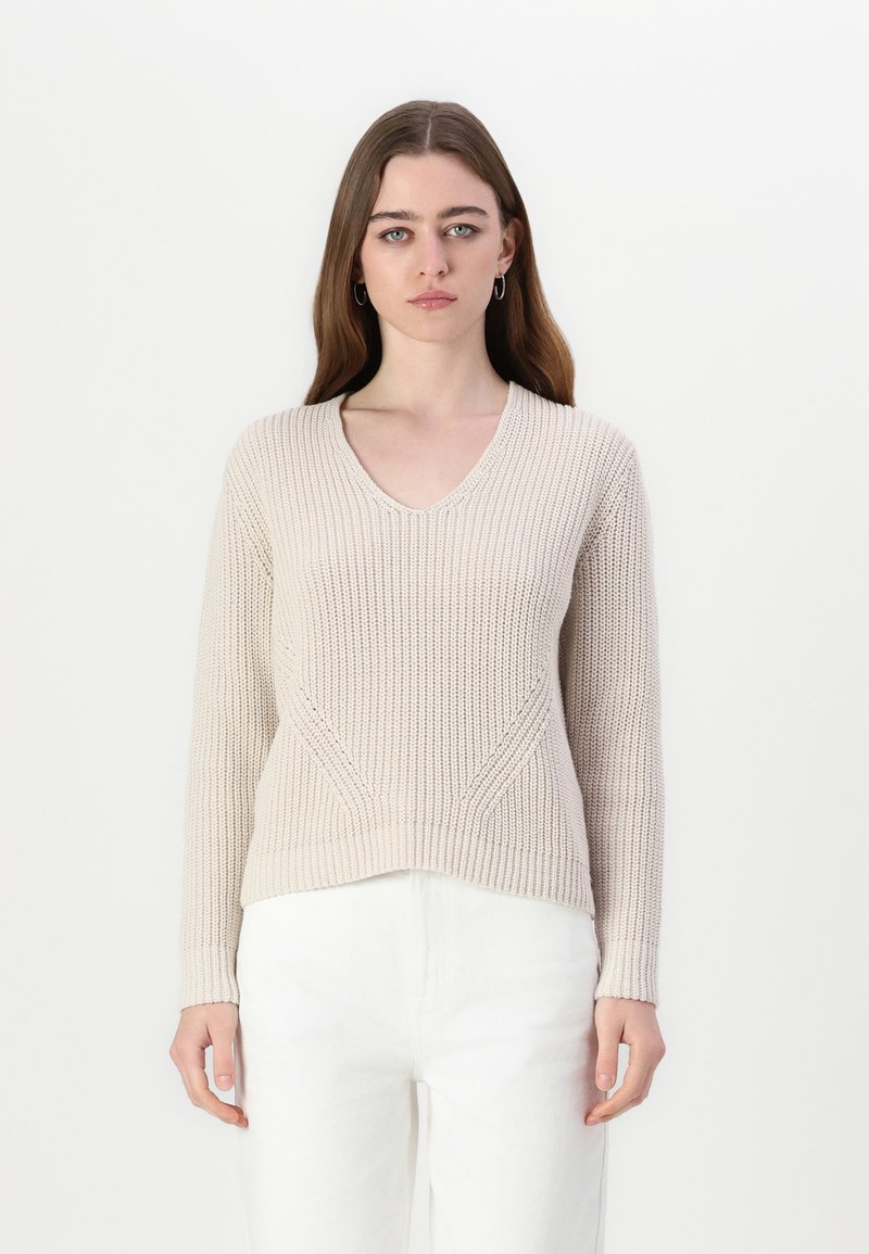 Pull en tricot beige avec un col en V, un motif texturé et des manches longues, présentant une coupe légèrement raccourcie et des poignets et un ourlet côtelés.