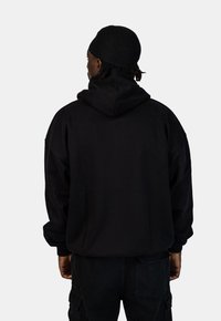 Zwarte oversized hoodie met een capuchon, met een zachte textuur, verlaagde schouders en geribde manchetten. G gedragen met donkere cargobroek.
