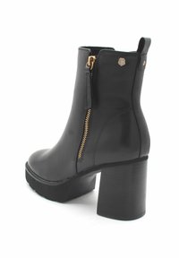 Botín de cuero negro hasta el tobillo con tacón grueso, cremallera lateral dorada y asa en la parte trasera, visto desde el lado trasero.