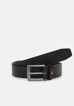 Black leather belt rolled with a square silver buckle and a small rectangular flag emblem on the loop.