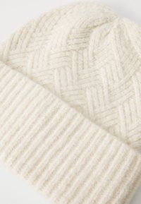 Gorro de lana de color crema tejido, con puño acanalado doblado y patrón trenzado texturizado en la parte superior.