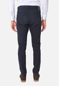 Pantaloni in cotone slim-fit blu navy con due tasche posteriori e un'etichetta sulla cintura, abbinati a scarpe in suede marroni.