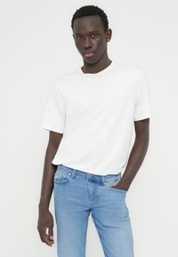 Λευκό βαμβακερό T-shirt με στρογγυλή λαιμόκοψη και κοντά μανίκια, σε συνδυασμό με τζιν παντελόνι σε ανοιχτό μπλε χρώμα, με τσέπες μπροστά και άνετη εφαρμογή.