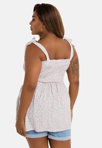 Top sin mangas floral con patrones en rosa y verde, cuerpo fruncido y tirantes ajustables; combinado con pantalones cortos de mezclilla.