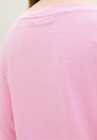 Light pink long-sleeve shirt featuring a scoop neckline and a smooth texture. Displaying a subtle logo on the back, crafted from soft fabric.
