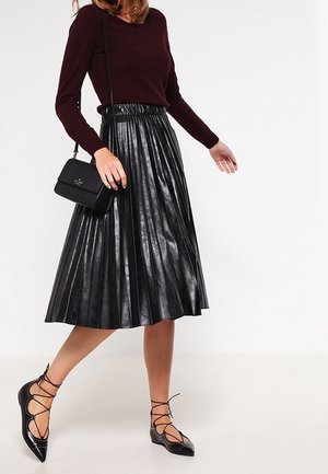 Musta pliseerattu nahkahame, jossa joustava vyötärönauha, yhdistettynä istuvaan viininpunaiseen neulepaitaan ja mustiin nyörikengännauhoihin. Pieni käsilaukku toimii korostuksena.