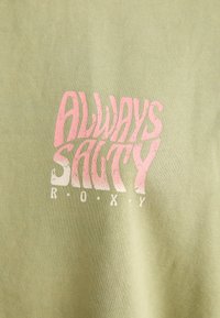 Tissu vert clair avec un texte rose et blanc disant "ALWAYS SALTY ROXY" dans une police ondulée et stylisée.