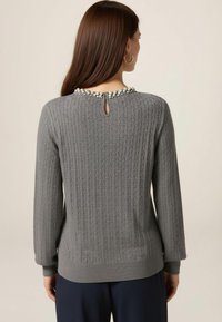 Šedý pletený svetr s texturovaným vzorem a perlovými ozdobami kolem otvoru ve tvaru klíče na zadním výstřihu. Dlouhé rukávy, žebrované manžety.