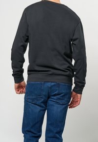 Svart sweatshirt med rund halsringning och långa ärmar, ihopparad med mörkblå denimjeans. Tyget verkar glatt och avslappnat.
