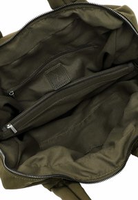 Interior de bolso tote verde oliva con compartimento con cremallera, tela suave y una etiqueta de cuero texturizada con detalle en relieve.