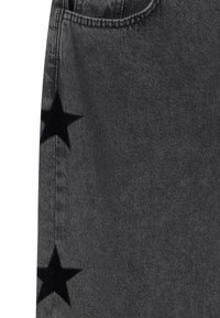 Tejido de mezclilla negra con dos parches de estrellas negras cerca de la costura y el borde de un bolsillo visible en la parte superior.