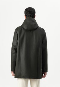 Σκούρο πράσινο αδιάβροχο μπουφάν με κουκούλα, παρουσιάζει άνετη εφαρμογή, μακριά μανίκια και λεία υφή. Επικεντρώνεται σε έναν καθαρό, μινιμαλιστικό σχεδιασμό.