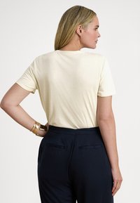 Κρεμ βαμβακερό μπλουζάκι με κοντά μανίκια, στρογγυλή λαιμόκοψη και άνετη εφαρμογή, συνδυασμένο με σκούρο μπλε παντελόνι με πίσω τσέπες.