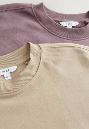 Dva crewneck dukseva složena jedan na drugi. Gore je u mekoj lavandinom nijansi; dolje je bež. Obojica imaju rebraste ovratnike, a oznake su vidljive unutar.