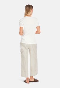 Weißes Baumwoll-T-Shirt, lockere Passform, kombiniert mit hellbeigen Leinen-Cargo-Hosen mit Seitentaschen und weitem Bein. Braune Slipper.