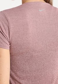 Camiseta deportiva Nike de color rosa con mangas cortas, que presenta un patrón texturizado y un pequeño logo plateado en la parte superior de la espalda.