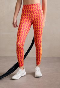 Leggings con un vivace motivo geometrico in rosa e arancione, design a vita alta e strisce laterali; abbinate a scarpe sportive bianche.