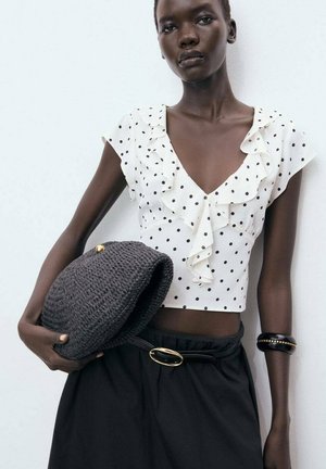 White polka dot blouse with ruffle detail, paired with a black skirt and a textured dark gray woven bag. Features a gold belt buckle accent.