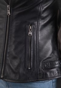 Black leather jacket featuring silver zippers, a smooth texture, and a side pocket with decorative stitch detail.