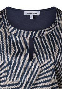 Navy blouse with a geometric pattern in beige and white, featuring a keyhole neckline, smooth texture, and rounded collar. Brand label visible.