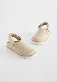 Chaussures slingback en toile beige avec une semelle en caoutchouc rose clair et des détails cousus. Design à talon ouvert avec une fermeture à strap ajustable.