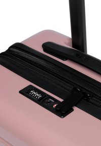 Valigia rigida rosa con cerniera nera e lucchetto a combinazione, caratterizzata da una superficie liscia e una forma rettangolare, progettata per i viaggi.