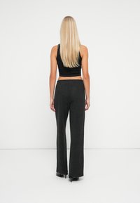 Kvinde med langt blond hår står med ryggen til, iført en sort ærmeløs crop top, kulfarvede vide bukser og sorte hæle.