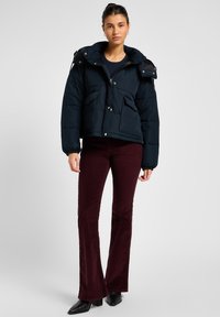 Navy puffer jacket with a hood, multiple front pockets, and silver hardware, paired with burgundy flared pants and black pointed heels.