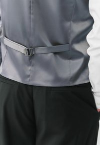 Szary satynowy kamizelka o wąskim kroju z paskiem z tyłu. Połączona z czarnymi spodniami, które mają gładką fakturę i staranne szycie.