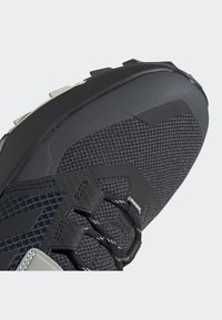 Schwarzer Sportschuh mit einer strukturierten Mesh-Oberfläche, verstärkter Zehenkappe und grauen Akzenten mit kontrastierenden Schnürsenkeln. Entworfen für Langlebigkeit.