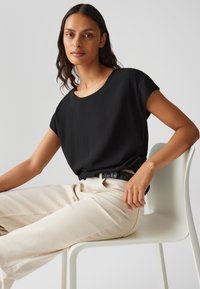 Top nero a maniche corte con scollatura rotonda, abbinato a pantaloni palazzo beige chiaro. Tessuto liscio e silhouette aderente, indossato con una cintura strutturata.