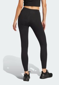 Svarta leggings med slät yta och hög midja, kombinerat med svarta träningsskor, sett från baksidan mot en ljus bakgrund.