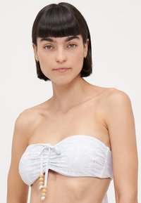 Banana-printed strapless bikini top in light pastel colors, featuring a gathered front, adjustable tie with beads, and smooth fabric texture.