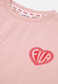 Ljust rosa bomulls t-shirt med korta ärmar, med en röd hjärt-logotyp som har texten "FILA" i vitt, samt en matchande röd etikett i nacken.