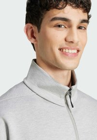 Ljusgrå, fleecejacka med dragkedja och hög krage, texturerat tyg, svart dragkedjedragare och en avslappnad passform. Minimalistisk design utan mönster.