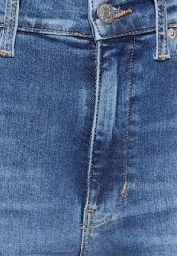 Jeans i medelblå tvätt med synliga blekningar, guldsydd, en metallknapp och femficka-design.