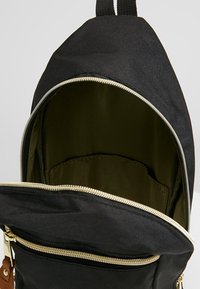 Zaino in tela nero con zip dorate; spazioso interno foderato in verde scuro; presenta una tasca esterna con zip e spallacci regolabili.