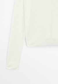 Pull blanc en tricot à manches longues montré de profil avec poignets et ourlet côtelés sur un fond blanc uni.