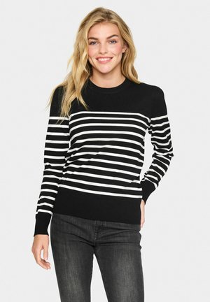 Maglione a righe bianche e nere con scollatura rotonda, polsini e orlo a coste, realizzato in un morbido tessuto a maglia. Abbinato a jeans scuri.