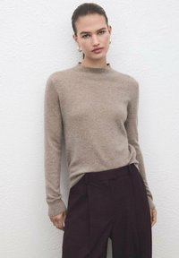 Jersey de cachemira beige con cuello redondo y mangas largas, combinado con pantalones de tiro alto de color púrpura oscuro con pliegues frontales.
