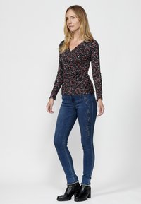 Langärmliges schwarzes Oberteil mit Blumenmuster, kombiniert mit eng anliegenden blauen Jeans mit floralem Stickerei und schwarzen Stiefeletten.