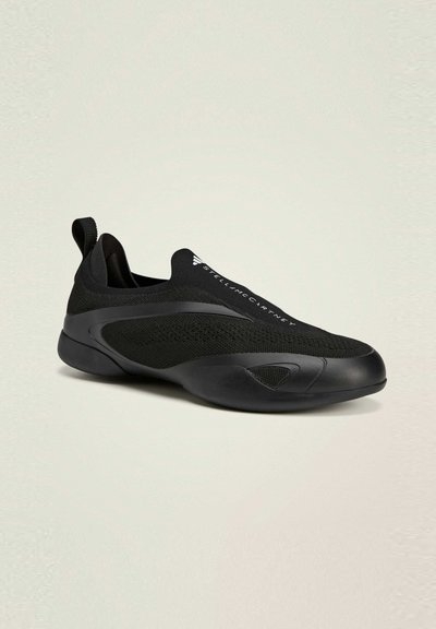 Black slip-on sneaker with a textured fabric upper, curved rubber sole, and subtle branding. Features a seamless design and pull tab.