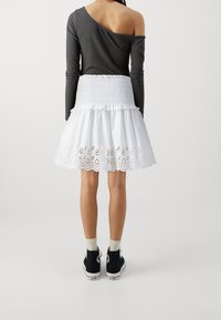 Grijs topje met één schouder, witte rok met smockwerk en kanten patroon langs de zoom, en zwarte sneakers met witte zolen en accenten.