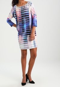 Barevné šaty s vzorem volného střihu, s lodním výstřihem a tříčtvrtečními rukávy. Tkanina vypadá lehká a hladká.