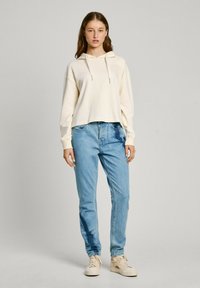 Sudadera corta de color crema con cordón. Pantalones vaqueros rectos de color azul claro con un patrón desgastado. Zapatillas de color beige claro.