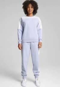 Šviesios levandų spalvos džemperis ir derančios kelnės iš minkštos medžiagos, su baltomis detalėmis ir laisvo kirpimo dizainu.